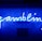 A bright blue neon sign spells out the word 'gambling' in cursive script. The background features a textured wall covered in domino tiles, also illuminated by the blue light, creating a vivid and visually striking scene.